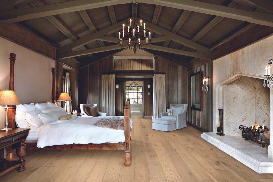white oak flooring in rustic ski cabin bedroom with vaulted wooden beams, chandelier, and stone fireplace